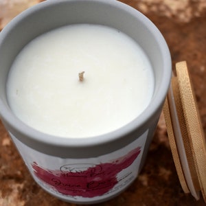 May include: A gray ceramic candle jar with a white wax candle and a wooden lid. The candle jar has a pink and white label with the text "Disco Fever" on it.