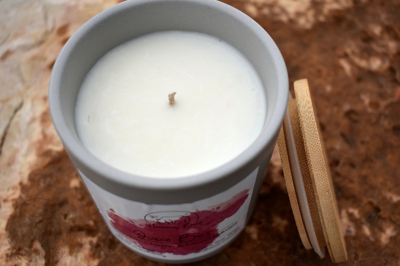 May include: A gray ceramic candle jar with a white wax candle and a wooden lid. The candle jar has a pink and white label with the text "Disco Fever" on it.