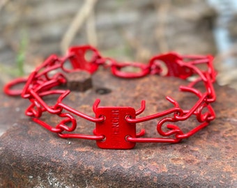 May include: A red prong collar for dogs. The collar is made of metal links and has a buckle closure. The collar is labeled "HENGER".