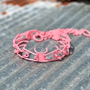 Puede incluir: Collar de púas rosa para perros. El collar está hecho de eslabones de metal y tiene una cadena.