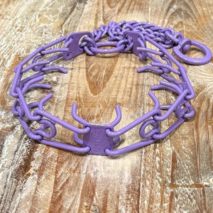 Puede incluir: Collar de púas morado para perros con un accesorio de cadena. El collar es de metal y tiene una etiqueta "SHOCK" en el lateral.