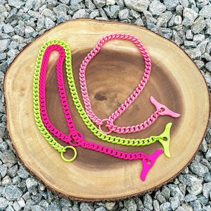 May include: Two neon chain necklaces, one pink and one green, with matching clasps. The necklaces are laid out on a wooden surface.