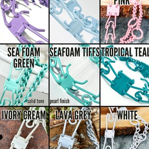 Op de afbeelding: Een set van negen hondenkettinghalsbanden in verschillende kleuren, waaronder lavendel, suikerspin, licht babyroze, zeeschuimgroen, zeeschuim, tropisch teal, ivoorcr&egrave;me, lavagrijze en wit. De halsbanden zijn gemaakt van metaal en hebben een springergesp.