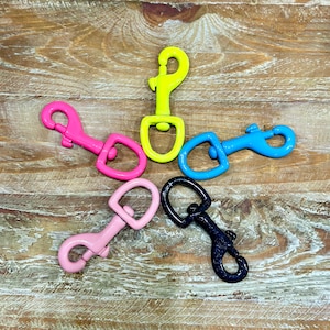May include: Five colorful metal clasps or hooks in pink, yellow, blue, black, and pink. The clasps are arranged in a star shape on a wooden surface.