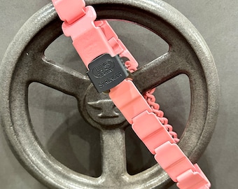 Op de afbeelding: Roze metalen ketting met een zwarte sluiting waarop "HS Germany SPRENGER" staat. De ketting is om een groot metalen wiel gewikkeld.
