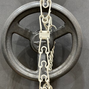 Puede incluir: Una rueda de metal gris con una cadena blanca unida a ella. La cadena tiene una etiqueta blanca con la palabra "SPRENGER" impresa en ella.