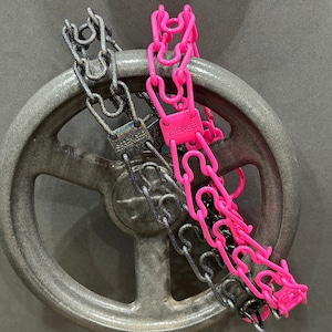 Puede incluir: Dos cadenas envueltas alrededor de una rueda de metal gris. Una cadena es negra y plateada, la otra es rosa y tiene la palabra "SPRENGER" en una etiqueta.