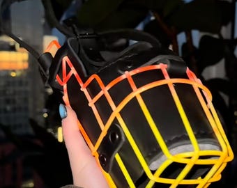 May include: A black leather dog muzzle with a bright orange and yellow wire cage. The muzzle is held in a hand.