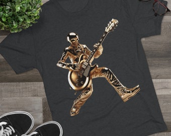 May include: A dark gray t-shirt with a gold-colored image of a person playing a guitar. The person is wearing a gold helmet and is in a dynamic pose.