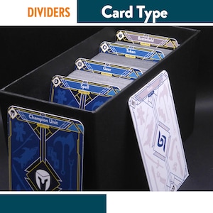 Pode incluir: Uma caixa preta para guardar cartas cheia de baralhos de cartas, separados por divisórias com as etiquetas "Champion Unit", "Spell", "Gear", "Token" e "Battlefield". Uma carta com um design branco está encostada na caixa. As palavras "DIVIDERS" e "Card Type" estão no topo.