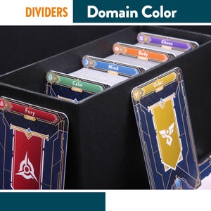 Pode incluir: Caixa preta com divisórias de cartas rotuladas como "Fury", "Calm", "Mind", "Body" e "Chaos". As cartas têm um design azul e dourado com uma faixa no topo. Os textos "DIVIDERS" e "Domain Color" estão na parte superior da imagem.