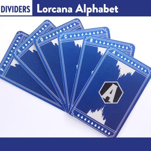 Pode incluir: Separadores de cartas azuis para o Alfabeto Lorcana, com detalhes e texto brancos. Cada carta apresenta uma letra do alfabeto, com um design estilizado. As cartas estão dispostas em forma de leque, com o texto "DIVIDERS Lorcana Alphabet" no topo.