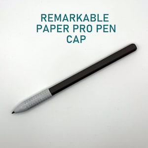 Könnte beinhalten: Eine Remarkable Paper Pro Stiftkappe mit einem dunkelbraunen, sechseckigen Körper und einem hellgrauen, texturierten Griffbereich an der Spitze. Der Text REMARKABLE PAPER PRO PEN CAP ist in Türkis über der Stiftkappe auf weißem Grund gedruckt.