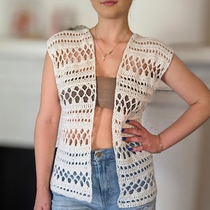 May include: A white crochet vest with a delicate openwork pattern. The vest has a V-neck and sleeveless design.