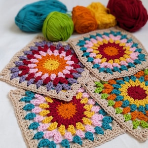 May include: Four colorful crocheted granny squares with a central circle design in shades of red, orange, yellow, green, blue, and purple. The squares are made with beige yarn and are arranged on a white surface.