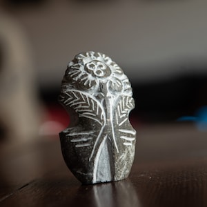 May include: A small, carved stone sculpture of a stylized flower with white details on a dark gray background.