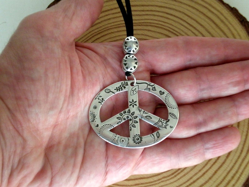 May include: A silver peace sign pendant necklace with a black cord and decorative beads. The peace sign is engraved with a floral pattern.