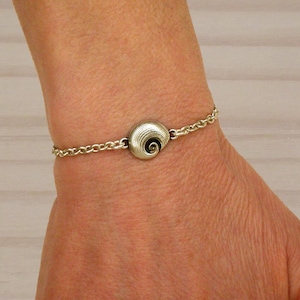 Op de afbeelding: Een zilveren kettingarmband met een zilveren bedel met een spiraalvormig ontwerp.