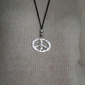 May include: A silver peace sign pendant necklace with a black cord. The pendant is detailed with small symbols and designs.