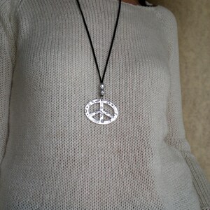 May include: A white knitted sweater with a silver peace sign pendant necklace.