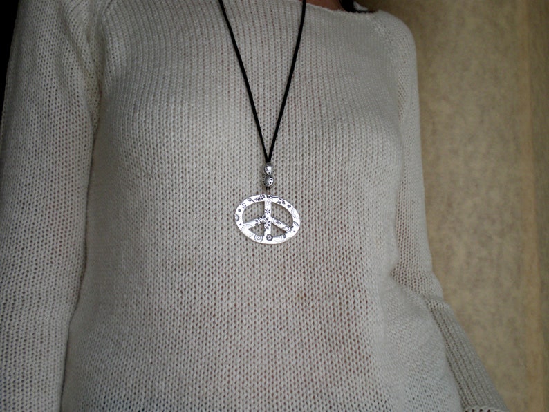 May include: A white knitted sweater with a silver peace sign pendant necklace.