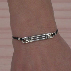 May include: A black cord bracelet with a silver charm featuring a geometric design.