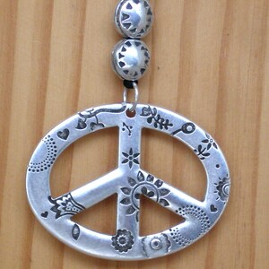 May include: A silver peace sign pendant with a detailed floral design. The pendant is attached to a silver chain with two silver beads.