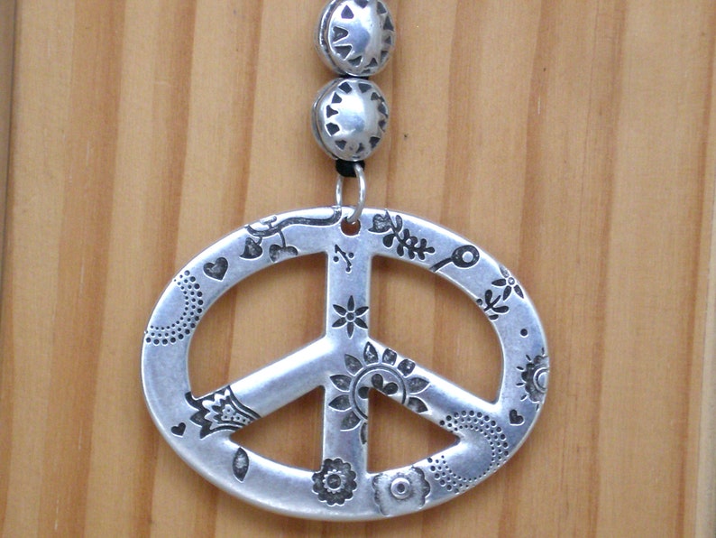 May include: A silver peace sign pendant with a detailed floral design. The pendant is attached to a silver chain with two silver beads.
