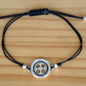 May include: A black cord bracelet with a silver button charm. The button has four holes and a raised design.