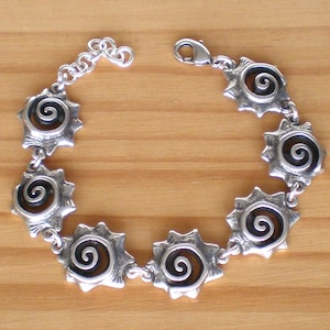 Op de afbeelding: Zilveren armband met een ketting en zeven zilveren bedels. Elke bedel heeft een zwart spiraalontwerp.