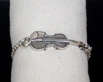 May include: A silver bracelet with a detailed violin charm. The charm is attached to a silver chain.