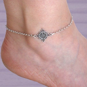 Peut inclure: Chevillère en argent avec un charme en nœud celtique. La chaîne est délicate et le charme est complexe.