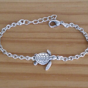 Puede incluir: Un brazalete de cadena de plata con un dije de tortuga de plata. El brazalete está hecho de una cadena delicada y el dije de tortuga está detallado con un caparazón texturizado.