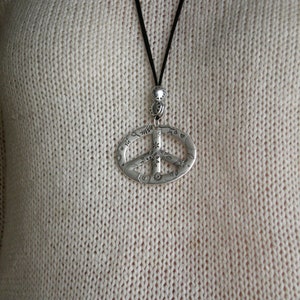 May include: A silver peace sign pendant necklace with a black cord. The pendant is detailed with small floral designs.