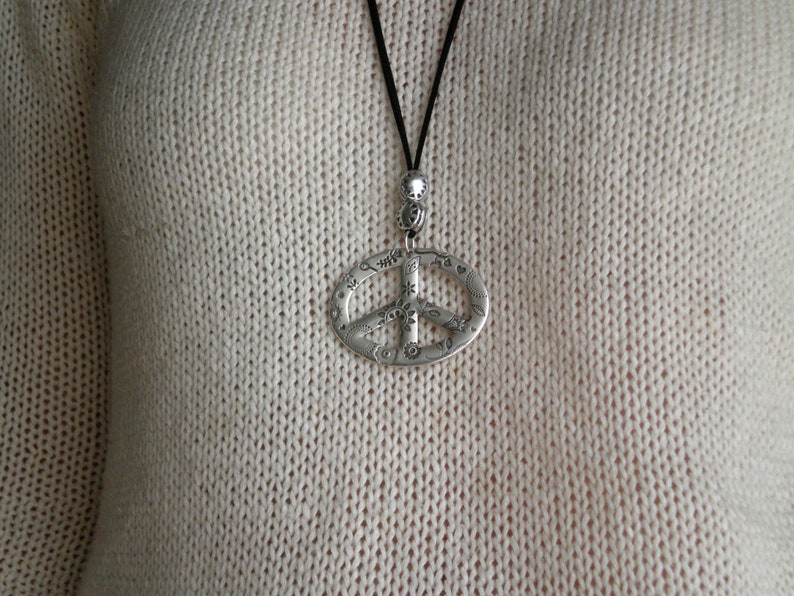 May include: A silver peace sign pendant necklace with a black cord. The pendant is detailed with small floral designs.