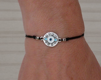 May include: A black string bracelet with a silver charm featuring a blue evil eye design.