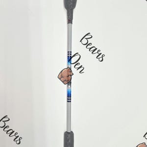 Könnte beinhalten: Eine Reitgerte mit einem grau strukturierten Griff und einem silbernen Schaft. Der Schaft hat blaue und schwarze Streifen. Der Text "Bears Den" ist im Hintergrund sichtbar.