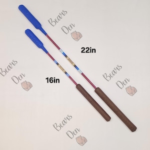May include: Two riding crops with blue textured ends and brown handles. The shafts feature red, blue, and gold decorative bands. One crop is labeled 16in and the other 22in. The text Bears Den with a bear icon is repeated across the background.