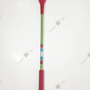 May include: A long, slender riding crop featuring a green shaft with a red leather handle and a matching red leather tip. The center of the shaft is decorated with a band of colorful, multi-striped geometric patterns.