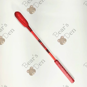 Könnte beinhalten: Eine rote Reitpeitsche mit genähtem Griff und Kopf. Der Schaft ist rot mit schwarzen und roten Streifen. Die Peitsche ist mit einem abgerundeten Kopf und einem rechteckigen Griff versehen.