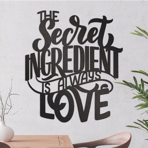 Puede incluir: Arte de pared de metal negro con el texto "The Secret Ingredient Is Always Love" en una fuente decorativa.