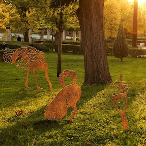 May include: Three rusty metal sculptures of an ostrich, a dog, and a bird in a grassy park setting. The sculptures are all facing the viewer and are made of a dark brown metal.
