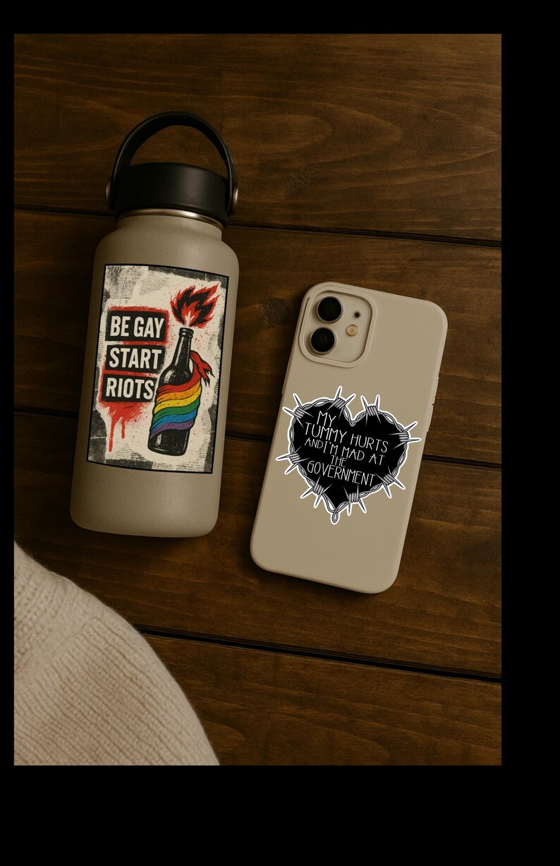 May include: A gray water bottle and a phone case with stickers. The water bottle has a sticker that says "BE GAY START RIOTS" with a rainbow and a bottle. The phone case has a sticker that says "MY TUMMY HURTS AND I'M MAD AT THE GOVERNMENT".