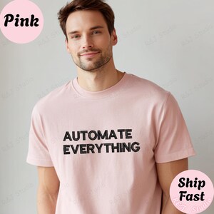 May include: A light pink short-sleeved t-shirt featuring the black embroidered text "AUTOMATE EVERYTHING" centered on the chest. The garment has a classic crew neckline and a standard fit, providing a clean and simple look for casual wear.