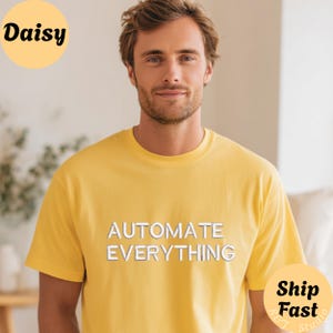 May include: A bright yellow short-sleeved t-shirt featuring the text "AUTOMATE EVERYTHING" printed in white block letters across the chest. The shirt has a classic crew neckline and a simple, clean design with no other visible patterns or graphics.