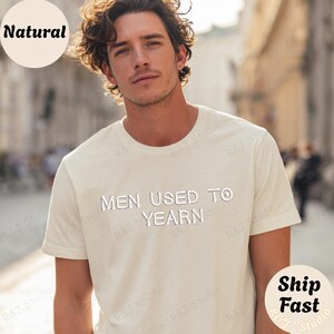 Può includere: Una t-shirt a maniche corte color crema con il testo "MEN USED TO YEARN" stampato in bianco con un carattere leggermente usurato sul petto. Il capo presenta un classico girocollo e una vestibilità standard, realizzato in tessuto tinta unita.
