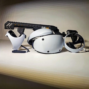 May include: A white virtual reality headset with two matching white controllers and a black rifle-style controller attachment. The black attachment features a top rail and the text EVIL printed in white on the side of the frame.