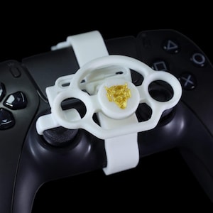 Op de afbeelding: Een witte 3D-geprinte stuuraanpassing voor een zwarte videogamecontroller. De aanpassing heeft een goudkleurig dierontwerp in het midden.