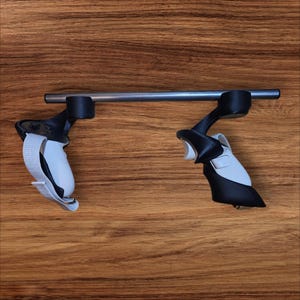 Może przedstawiać: Para czarno-białych kontrolerów zestawu słuchawkowego VR połączonych srebrnym prętem. Kontrolery mają białe paski i są umieszczone na drewnianym tle.