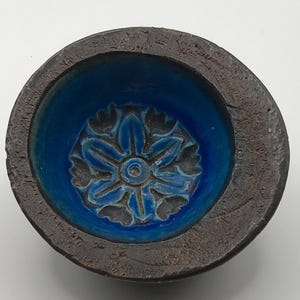 May include: A small blue ceramic bowl with a floral design. The bowl has a dark brown rim.